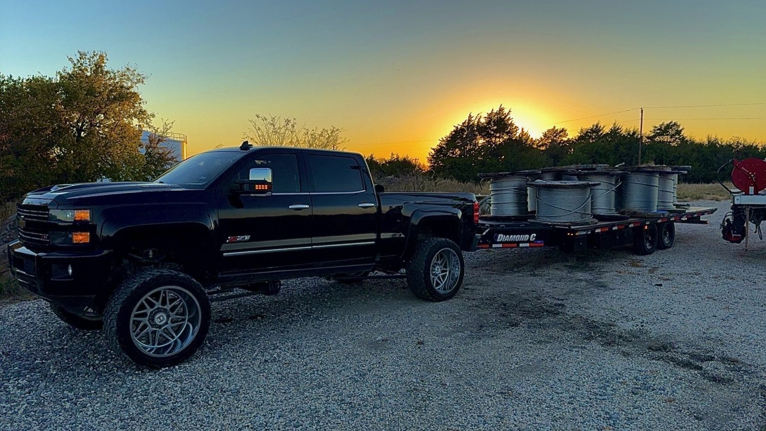 Tilt deck trailer rental hauling industrial cable spools behind pickup at sunset in Texas